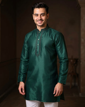 Man wearing a green kurta with white pants against a dark background