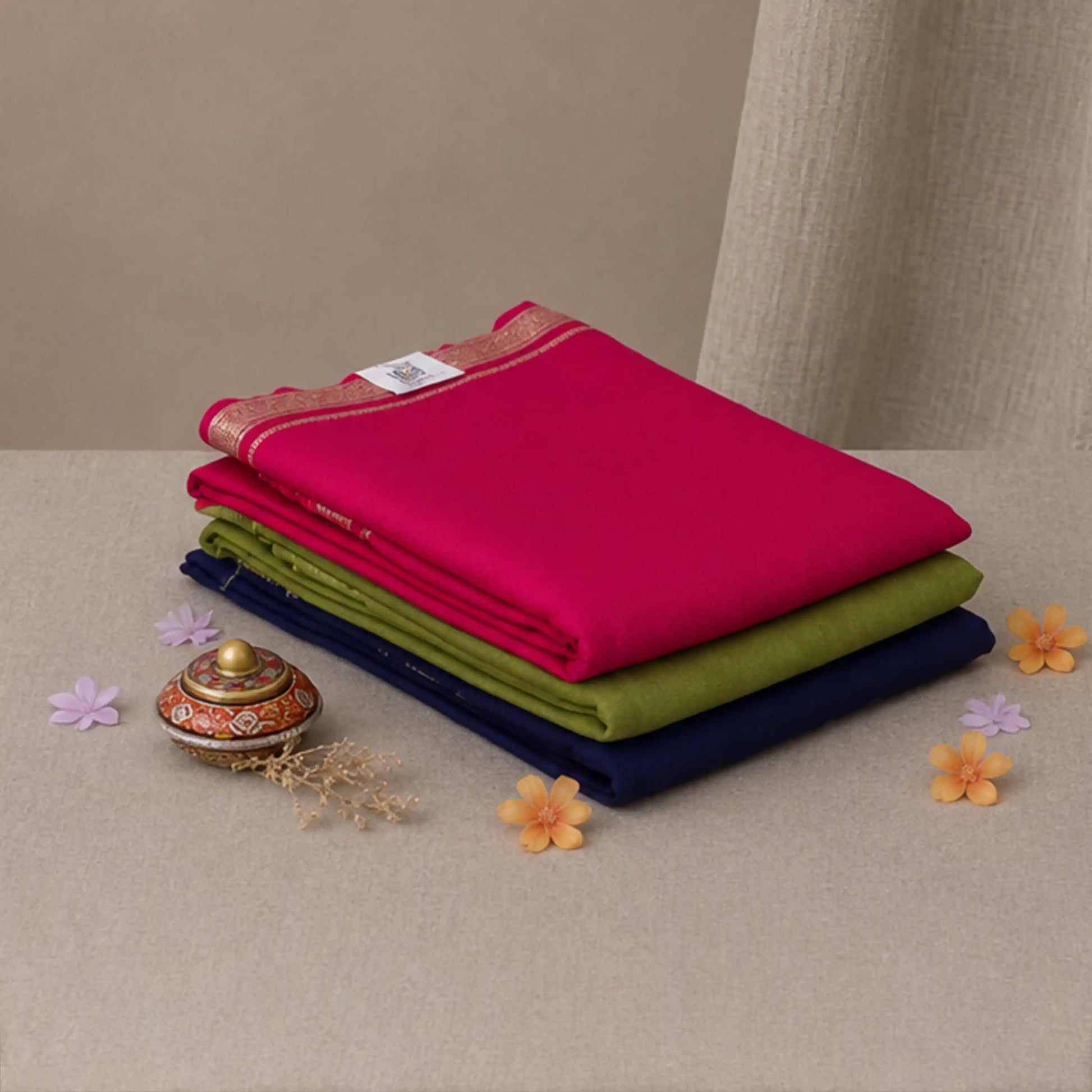 A stack of three folded fabric pieces in bright pink, olive green, and navy blue