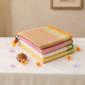 Stacked Mul Mul cotton sarees in pastel shades with woven borders and tassels,folded display front view
