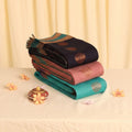 Elampillai silk cotton saree with gold woven butta motifs in navy, pink and teal shades folded stack close up view.