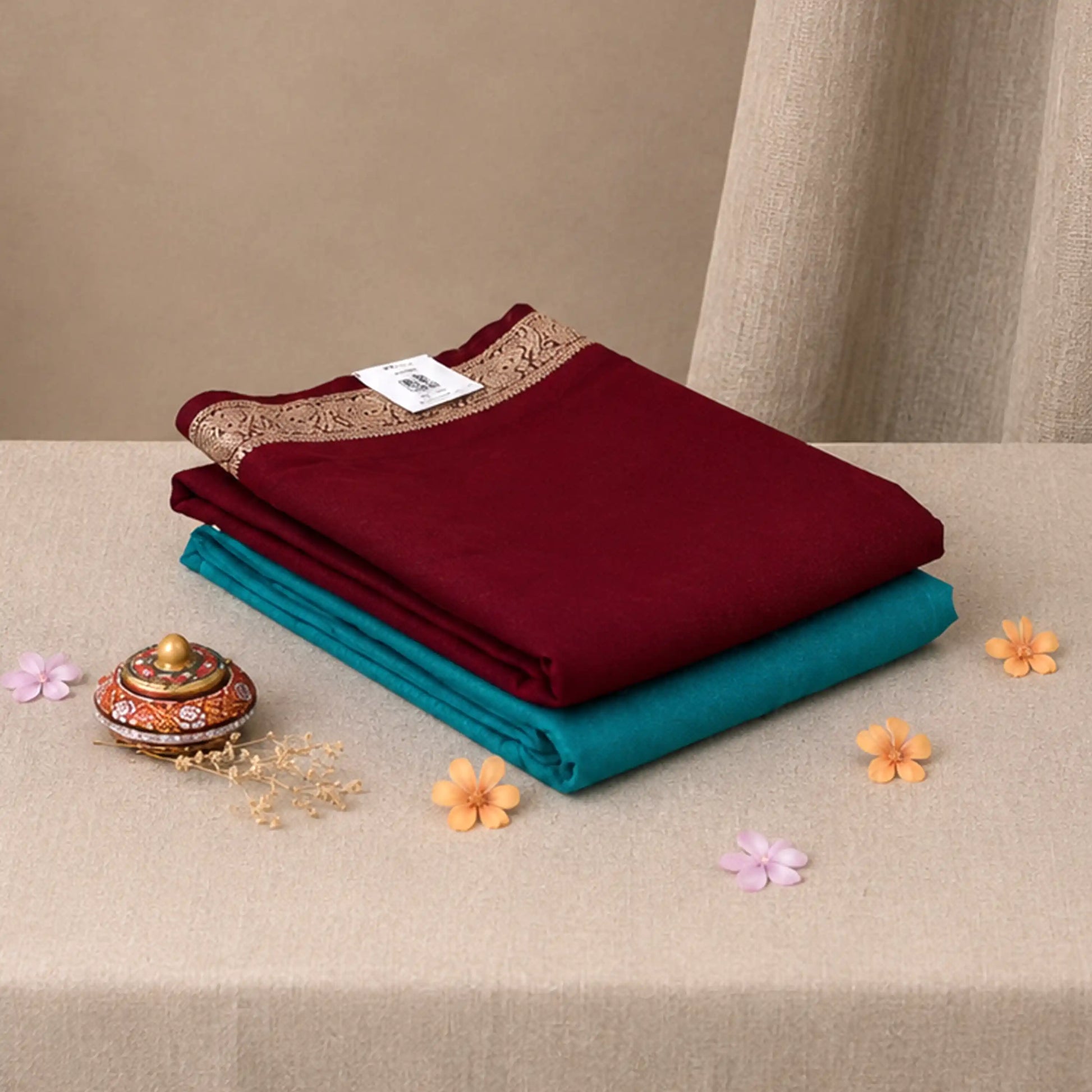 Folded Mysore Silk saree with plain maroon body, gold zari woven border and teal running blouse piece, top view.