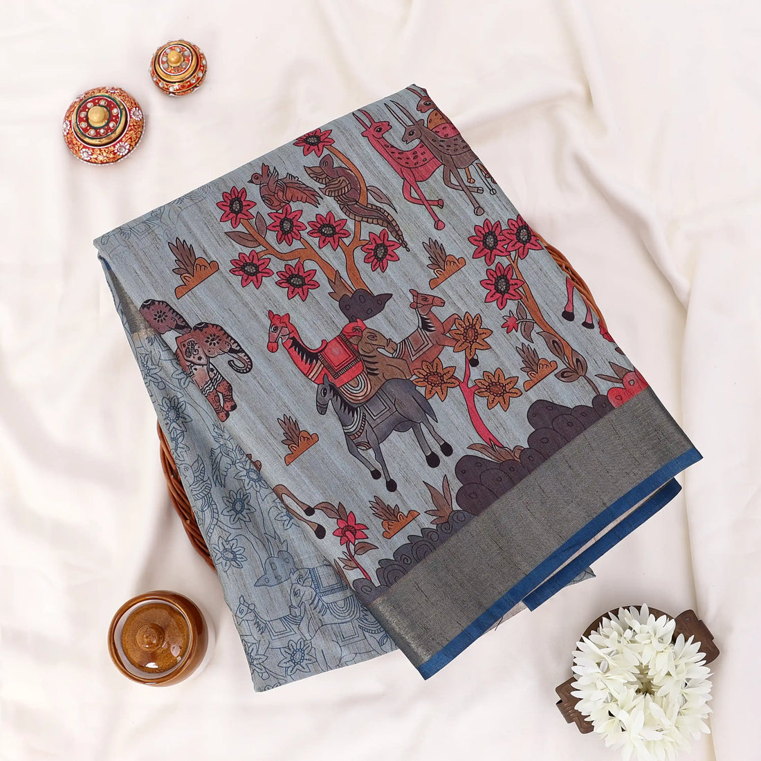 A grey and blue saree with red floral patterns and a metallic gold border.