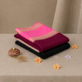 A stack of folded sarees in vibrant colors, featuring a bright pink saree with a gold border on top, followed by a  black saree. 