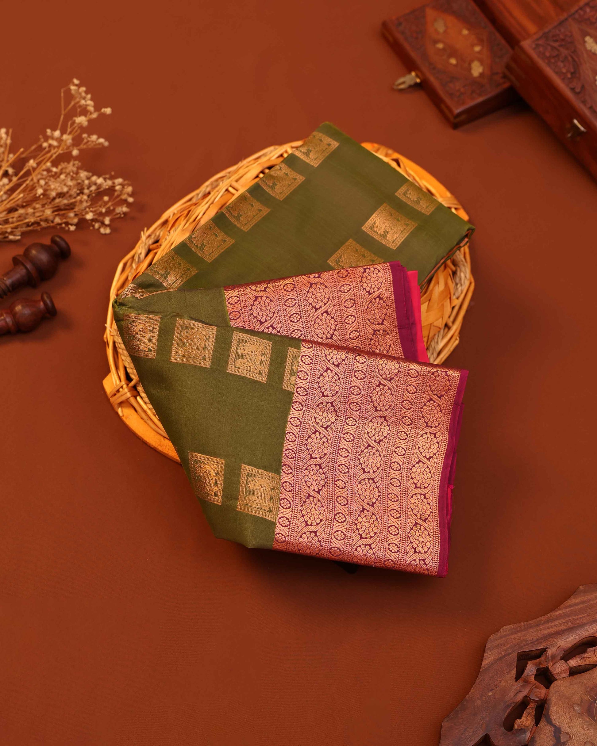 Two embroidered sarees in green and pink on a woven basket with a brown background