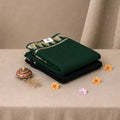 A stack of folded saree pieces, with the top piece in dark green and the bottom piece in black