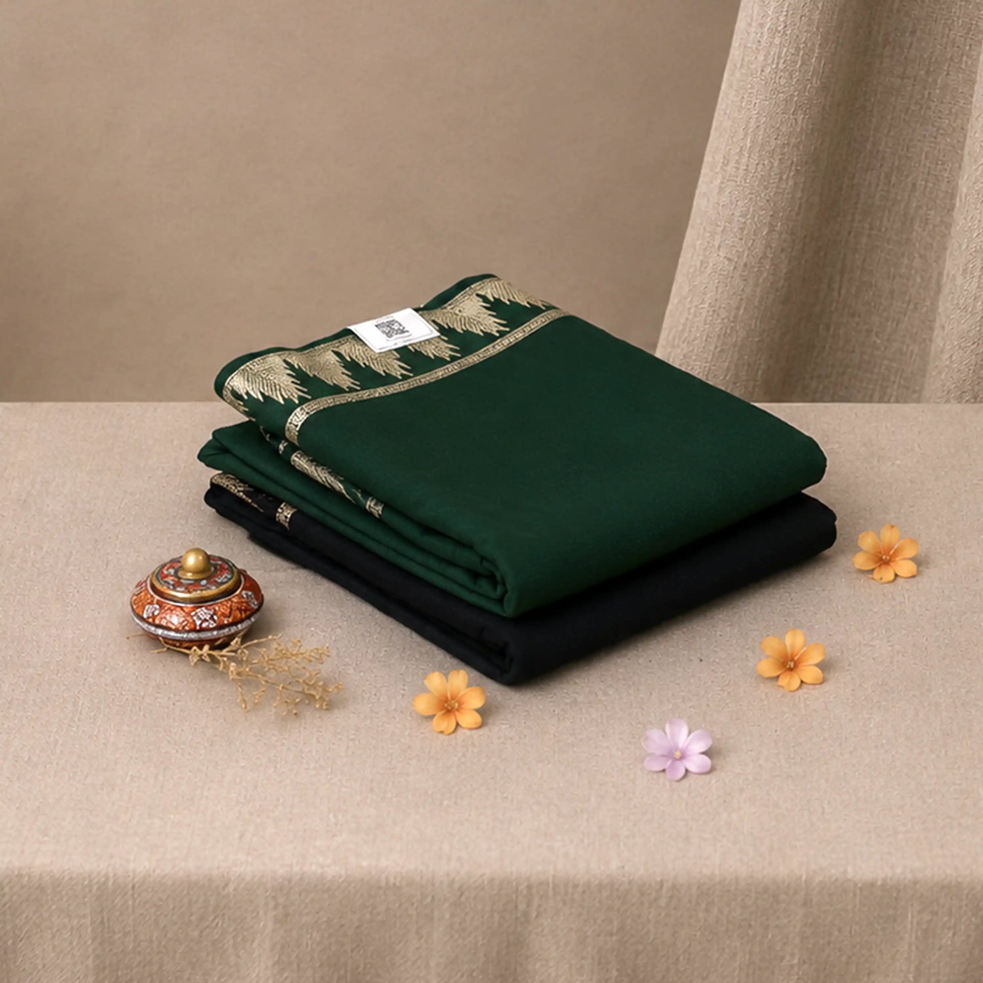 A stack of folded saree pieces, with the top piece in dark green and the bottom piece in black