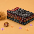 Semi Chanderi saree with intricate white floral print on black fabric maroon border folded stack front angled view.