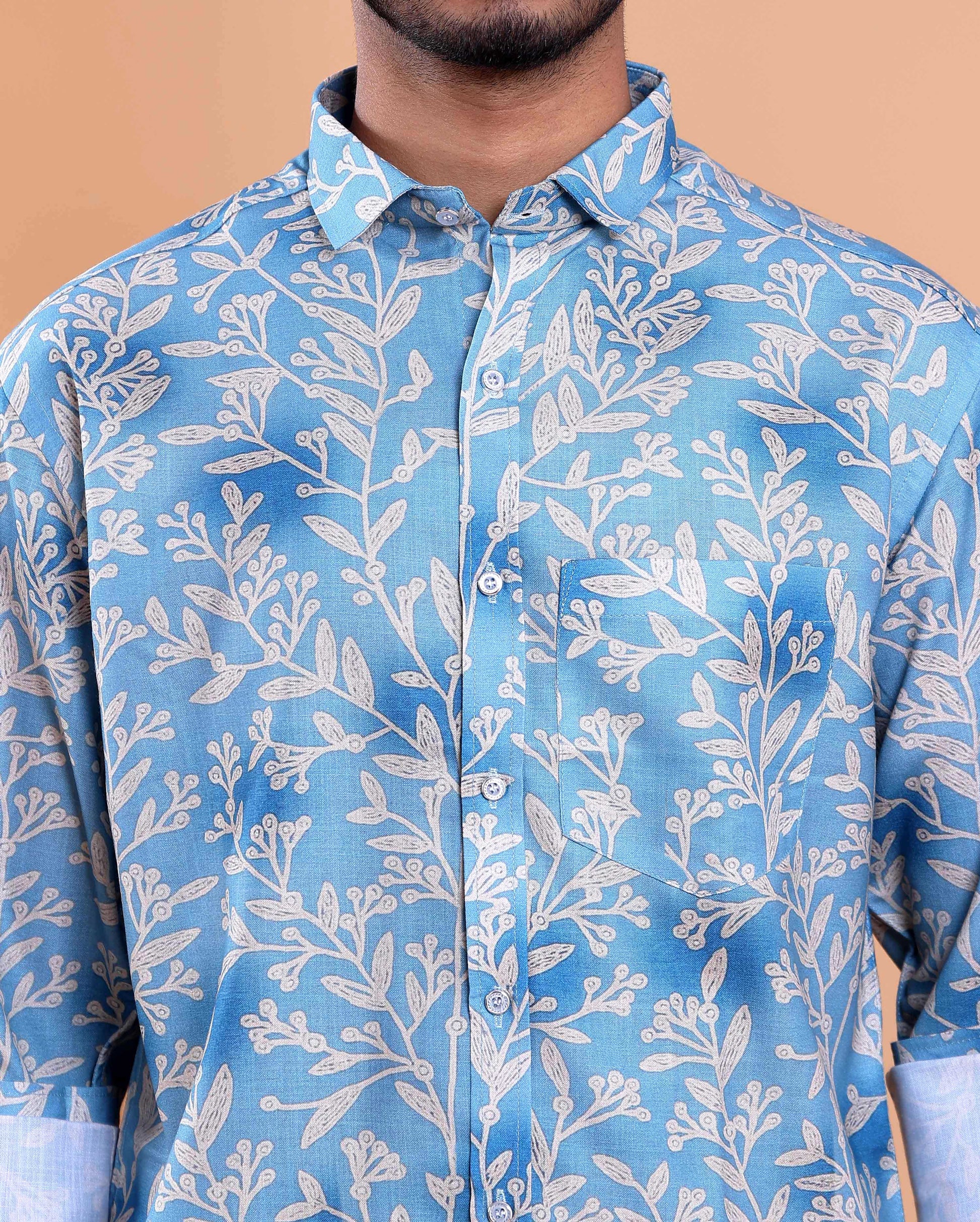 Blue shirt with white leaf pattern worn by a person against a beige background