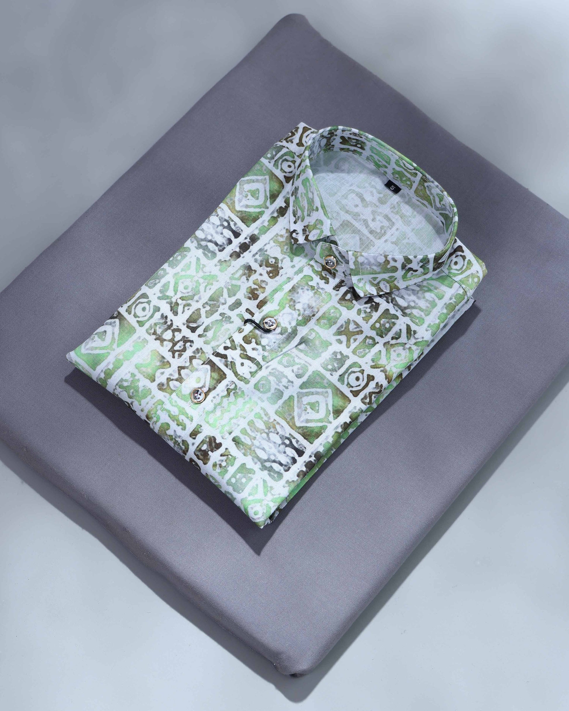 Folded shirt with green geometric pattern on a gray surface