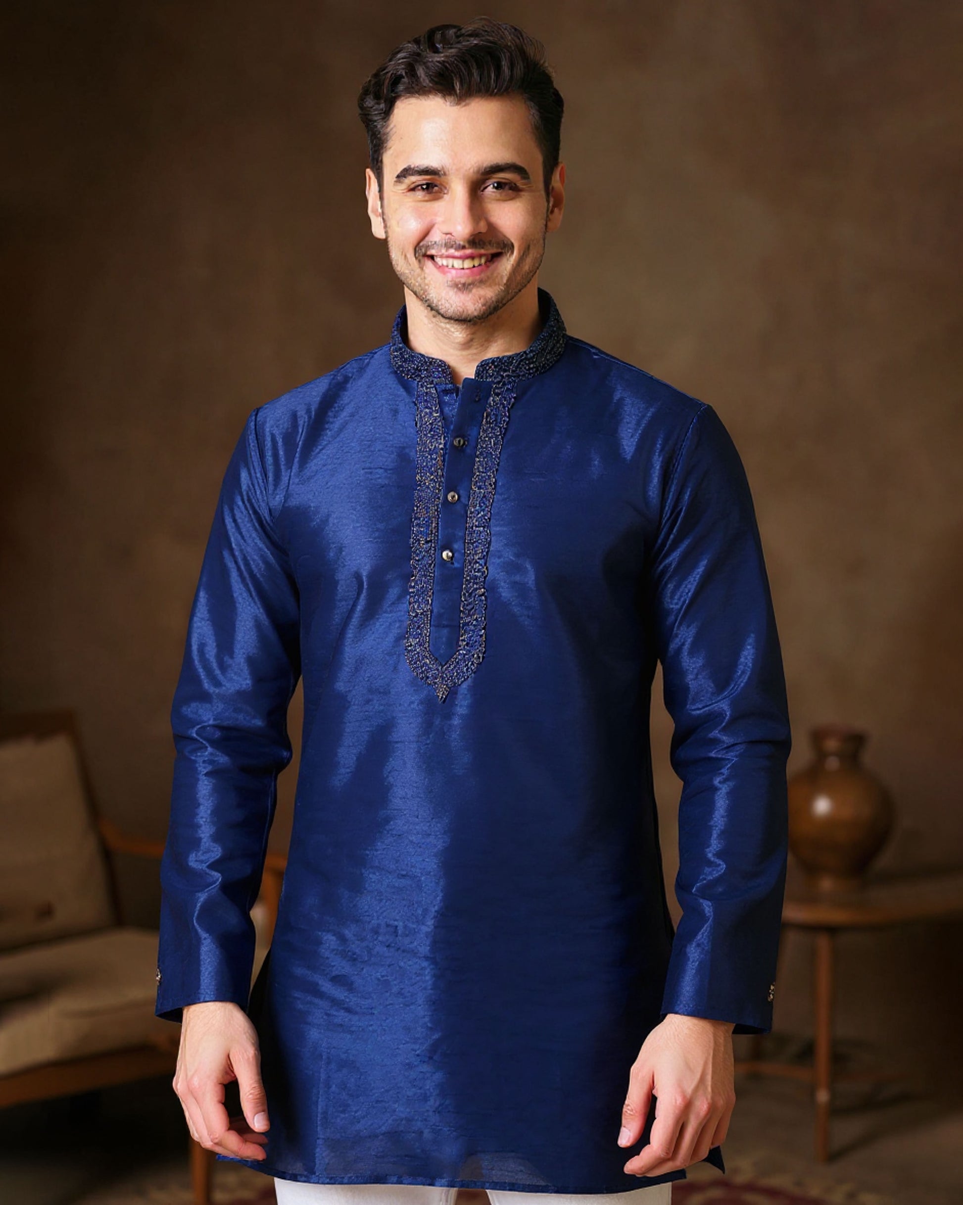 Man wearing a blue kurta with intricate embroidery against a warm-toned background