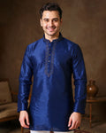 Man wearing a blue kurta with intricate embroidery against a warm-toned background