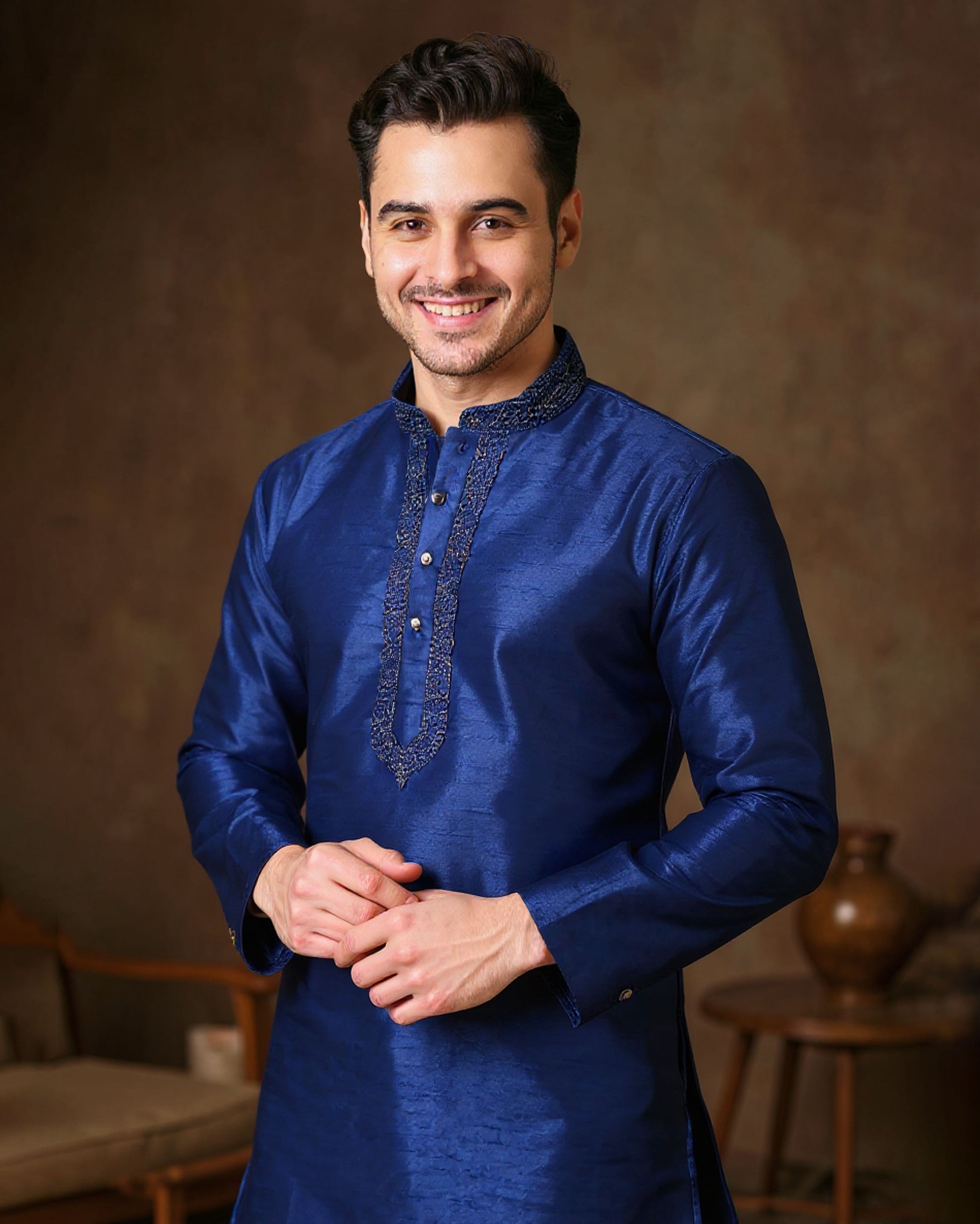 Man wearing a blue kurta with intricate embroidery against a brown background