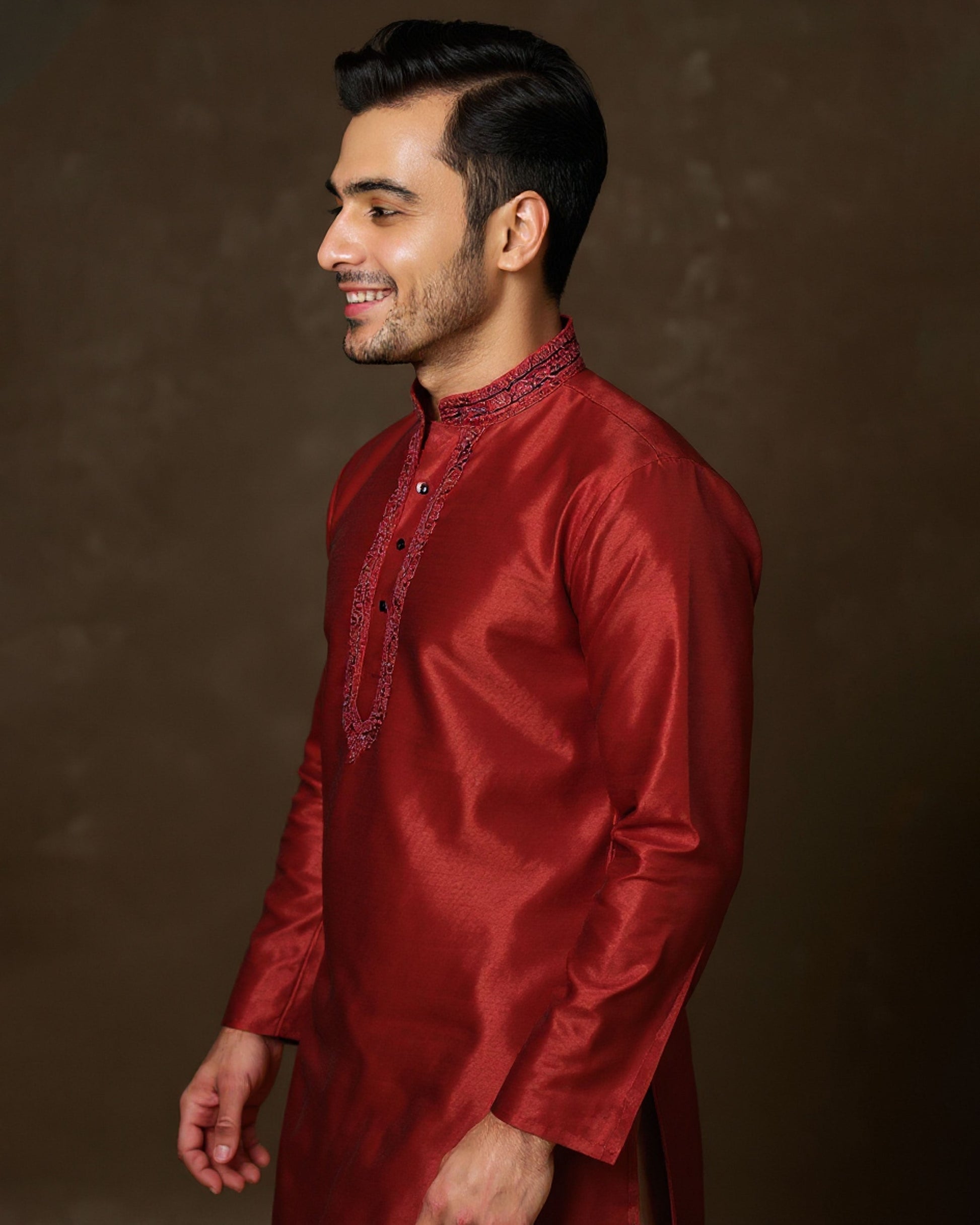 Man wearing a red traditional kurta against a brown background
