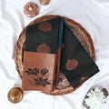 Elampillai silk cotton saree with floral zari border in dark green folded display on wicker basket top view.
