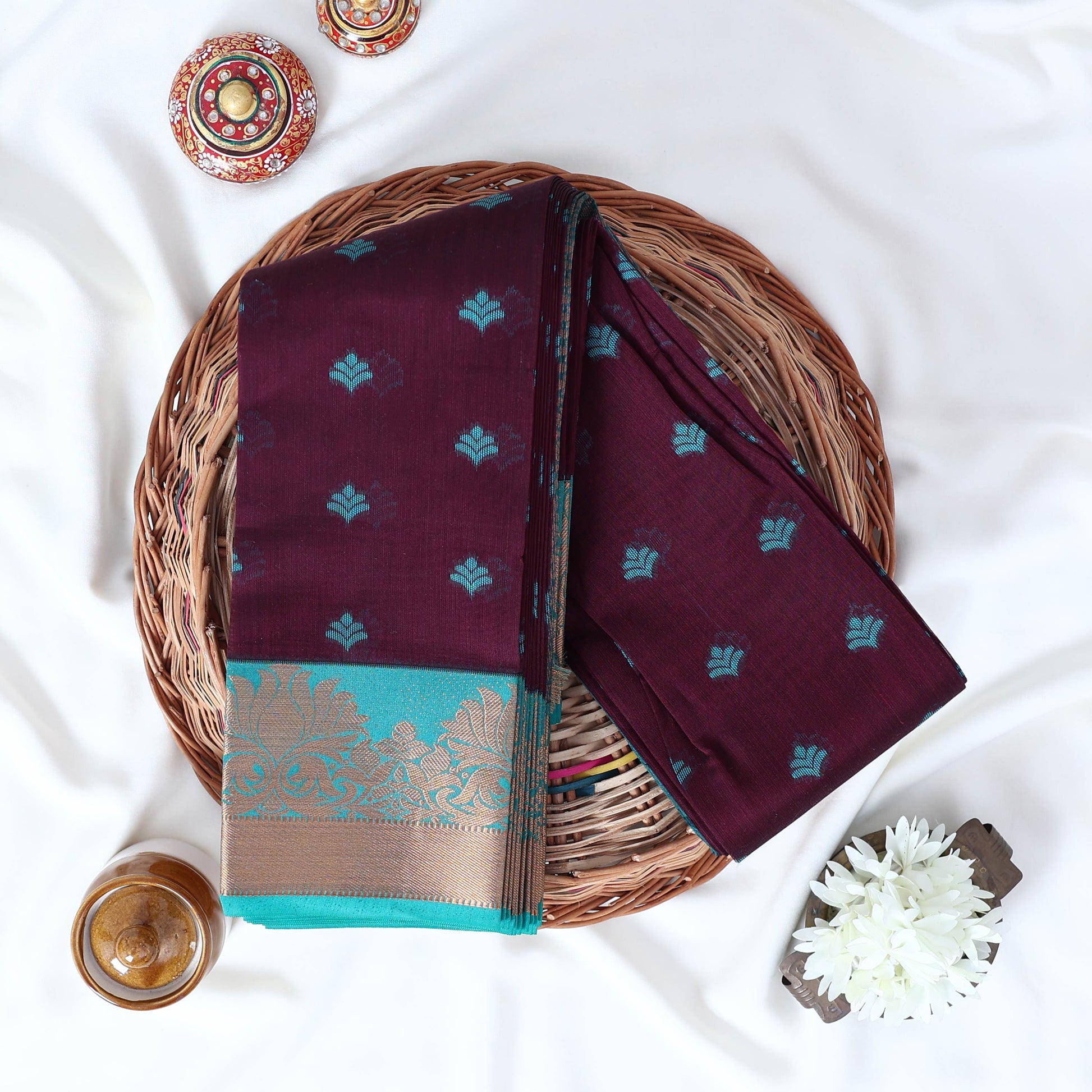 Purple Elampillai silk cotton saree with woven butta motifs and floral zari contrast border folded top view display.
