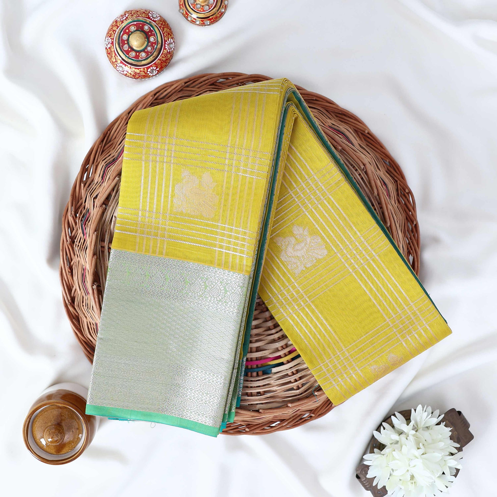 Elampillai silk cotton saree with floral butta checks pattern and floral zari border in green folded top view.