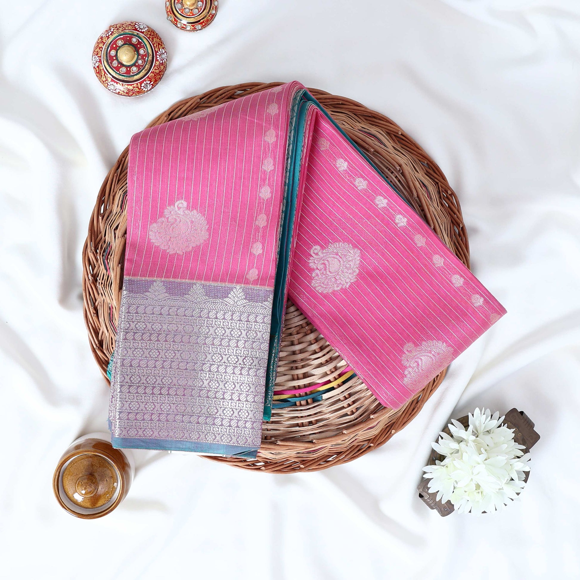 Light pink Elampillai silk cotton saree with silver zari floral buttas, vertical stripes and contrast floral zari border folded top view.