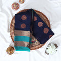 Elampillai silk cotton saree with floral butta motifs navy blue body and teal zari border folded top view on woven basket.