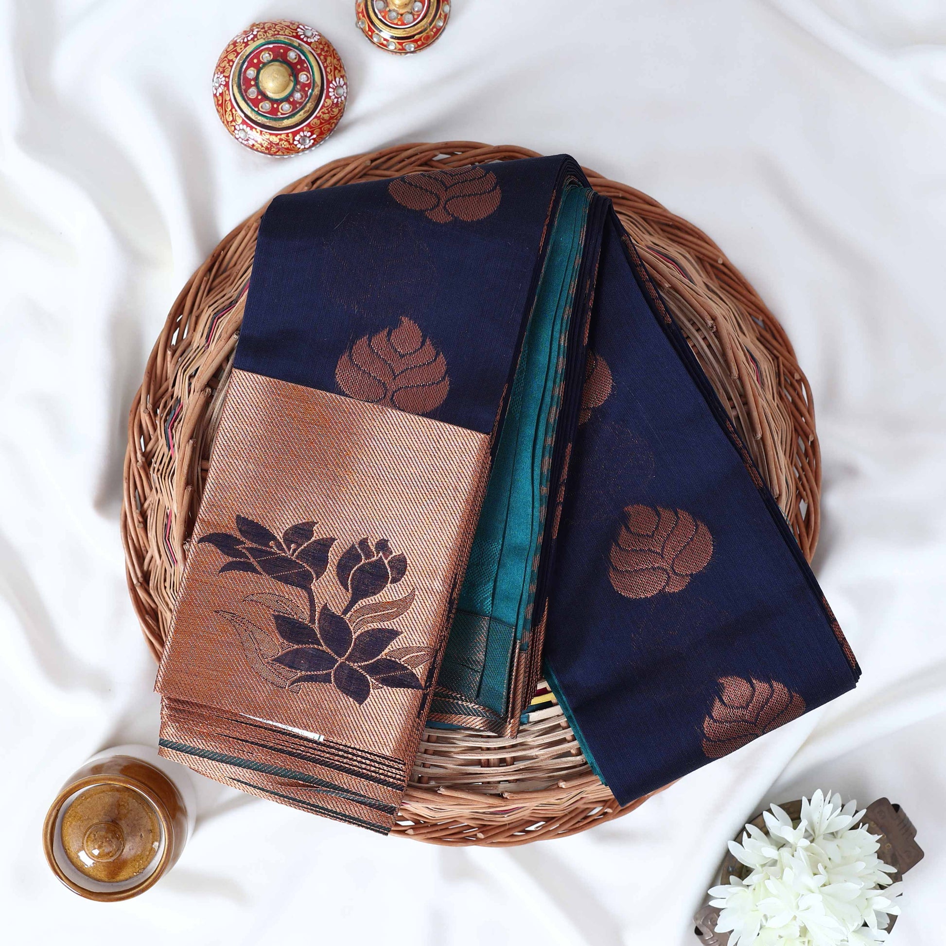 Elampillai silk cotton saree with floral zari border in navy blue folded top view on wicker basket display.