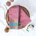 Elampillai silk cotton saree with floral butta motifs pink body and light blue zari border folded top view on woven basket.