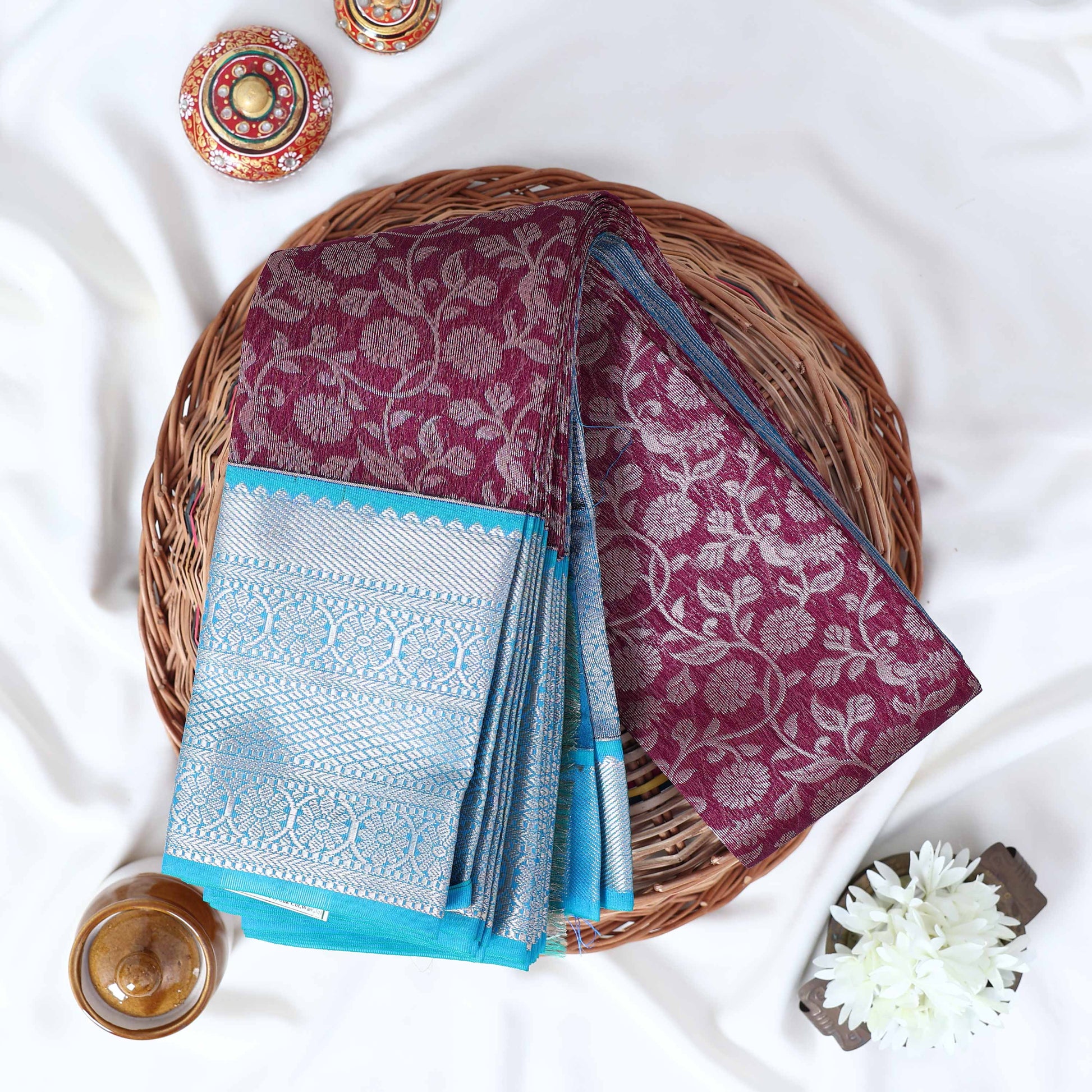 Elampillai silk cotton saree with leaf jaal woven purple body and turquoise chevron zari border folded top view.