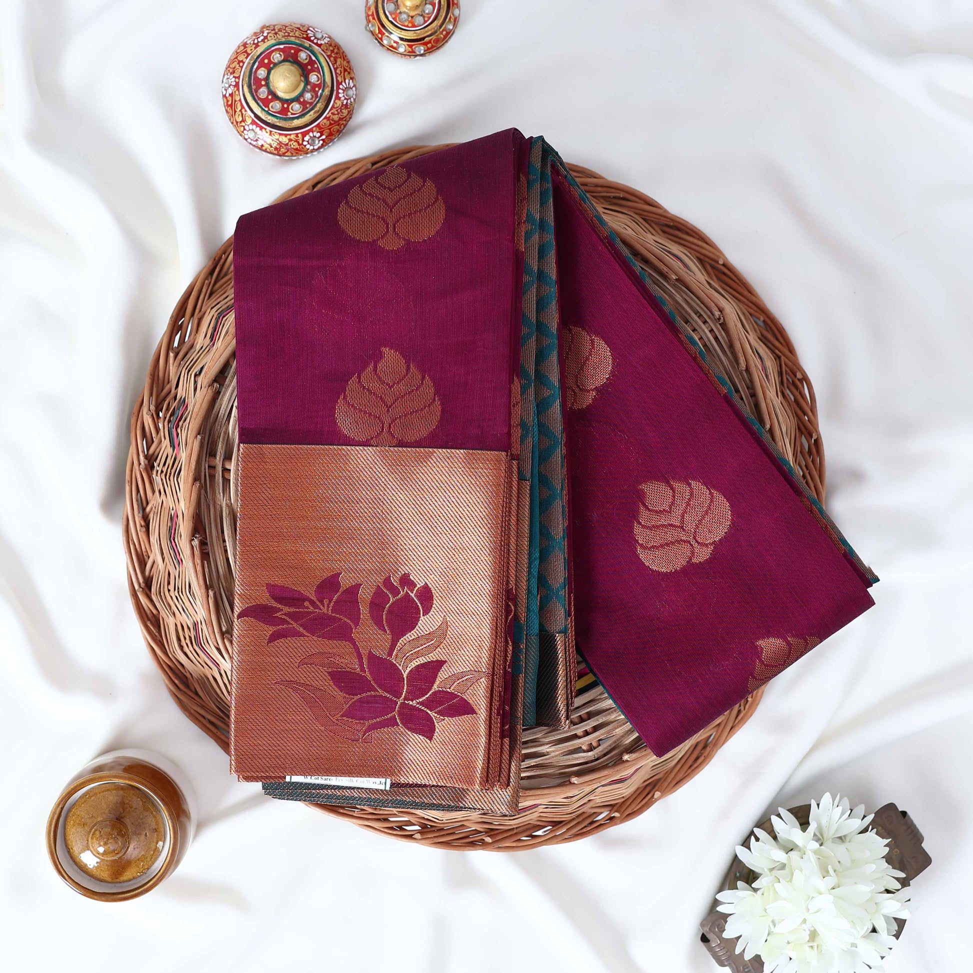 Elampillai silk cotton saree with floral zari border in purple folded display on wicker basket top view.