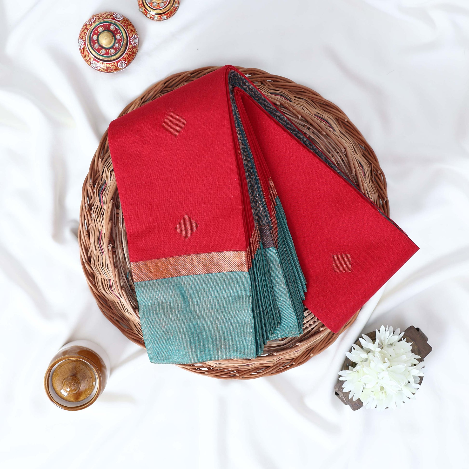 Red Elampillai silk cotton saree with gold zari buttas and contrast zari border, folded top view.