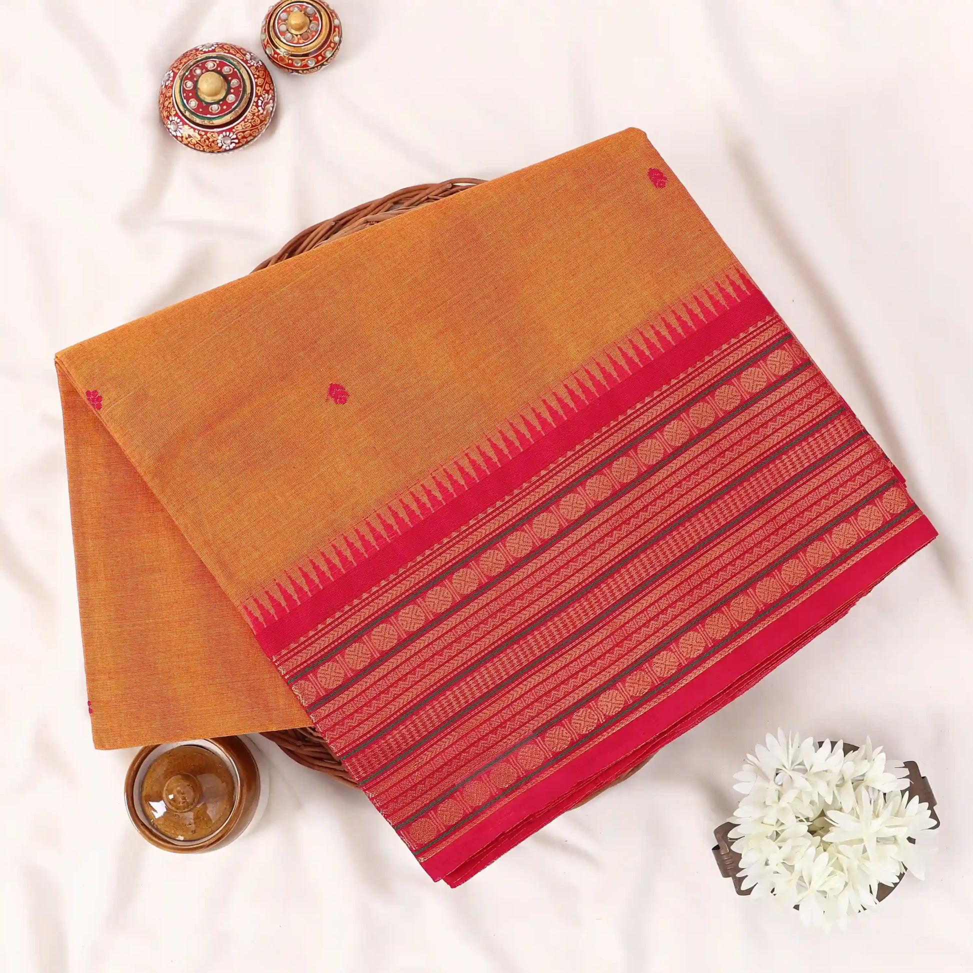 Chettinad cotton saree with orange plain body temple zari border and woven butta motifs folded top view.