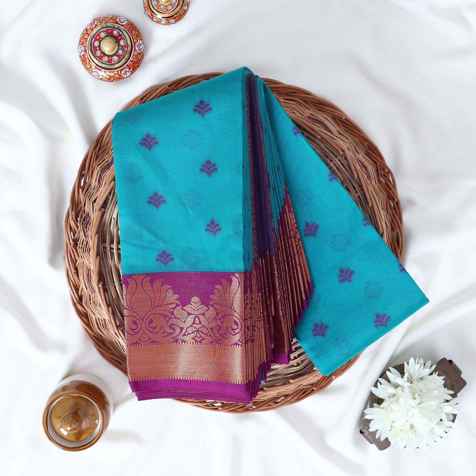 Teal Elampillai silk cotton saree with woven butta motifs and floral zari contrast border folded top view display.