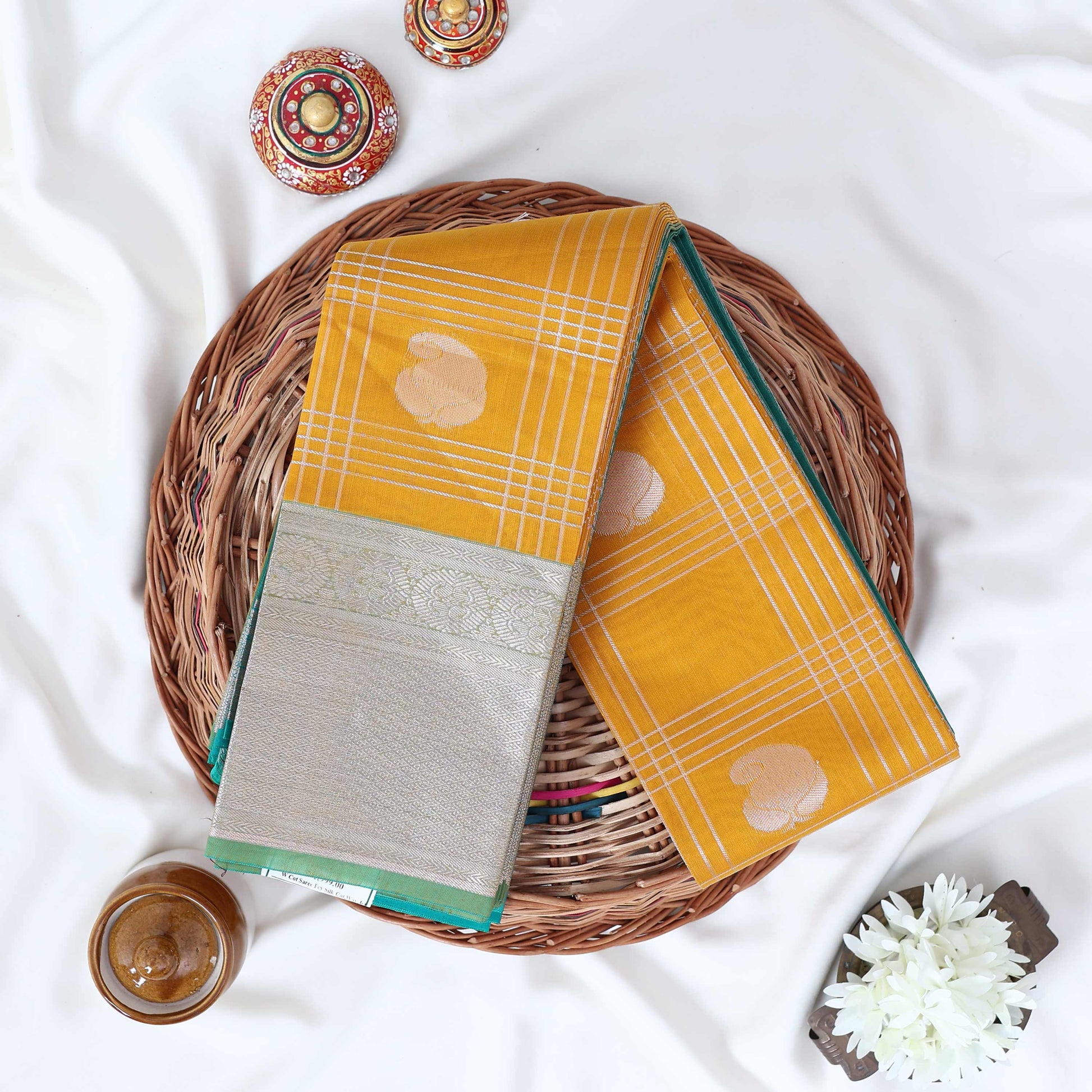 Elampillai silk cotton saree with floral butta checks pattern and floral zari border in yellow top view display.