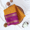 Elampillai silk cotton saree with yellow checked body and pink zari border folded flat lay view on woven basket.