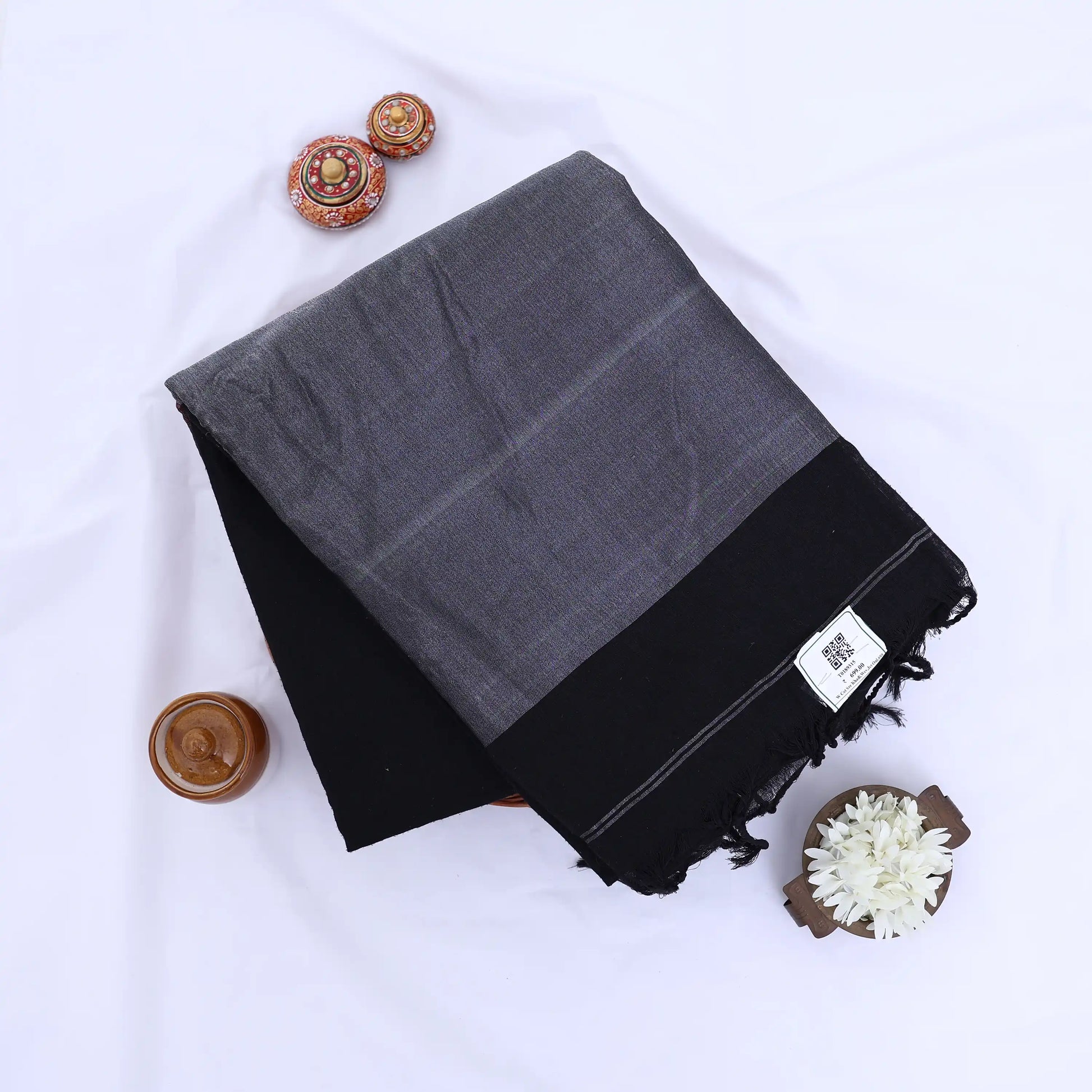 Khadi cotton saree with contrast woven border and tassels in black folded flat lay product view.