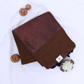 Khadi cotton saree with contrast woven border and tassels in brown folded flat lay product view.