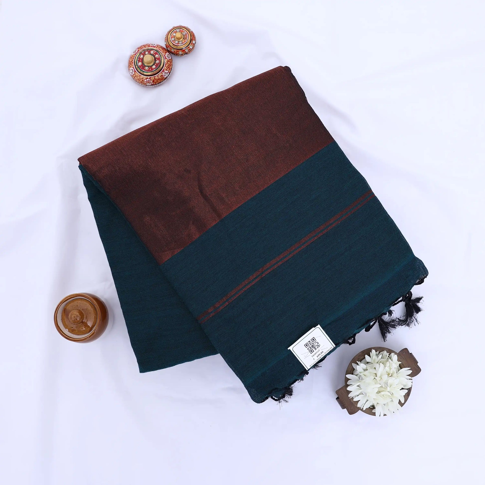 Khadi cotton saree with contrast woven border and tassels in teal folded flat lay product view.