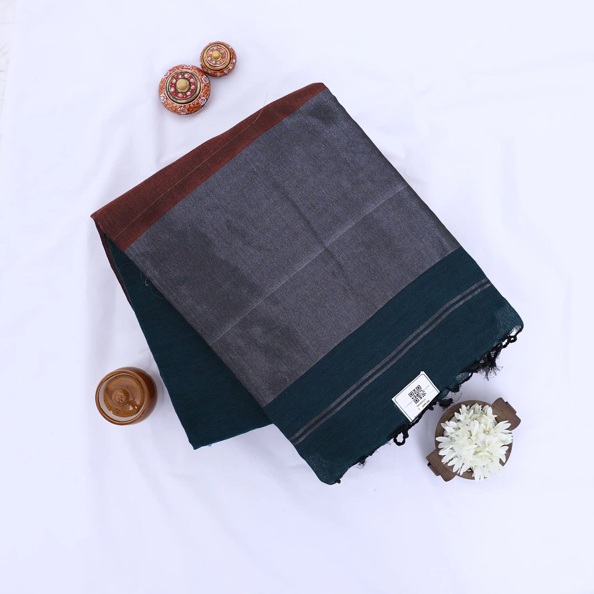 Khadi cotton saree with contrast woven border and tassels in dark teal folded flat lay product view.