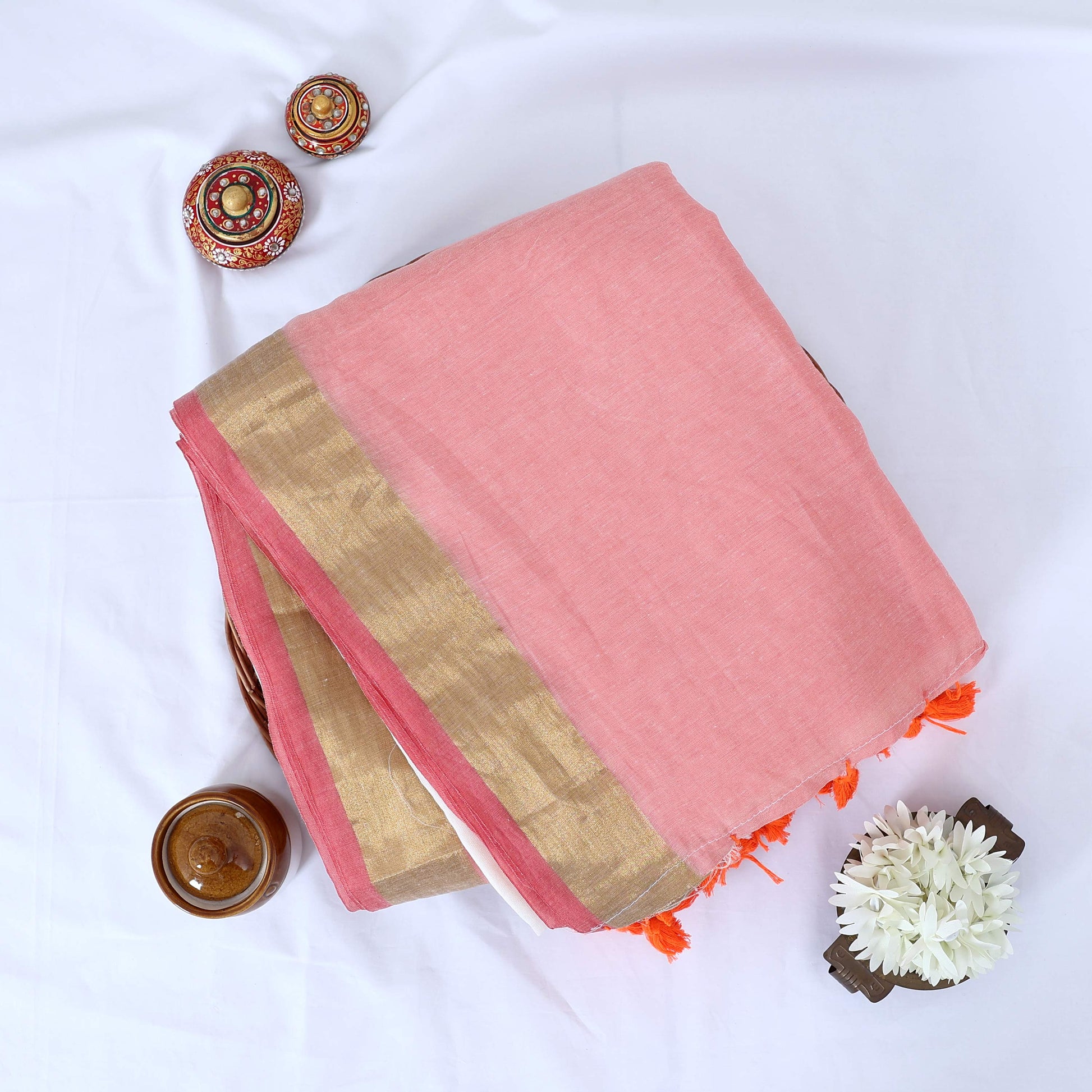 Mul Mul cotton saree with soft pink body gold zari border and orange tassels folded top view display