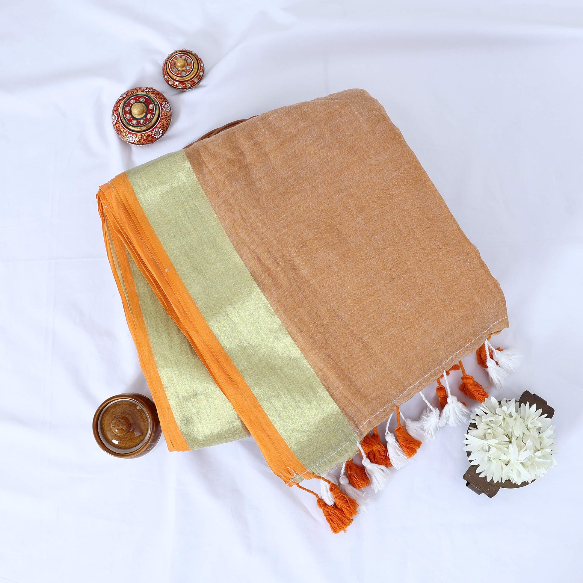 Mul Mul cotton saree with lighrt sandal body gold zari border and orange tassels folded top view display