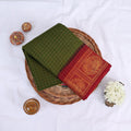 Sungudi cotton saree with gold zari checks body and green peacock motif border folded top view on wicker basket