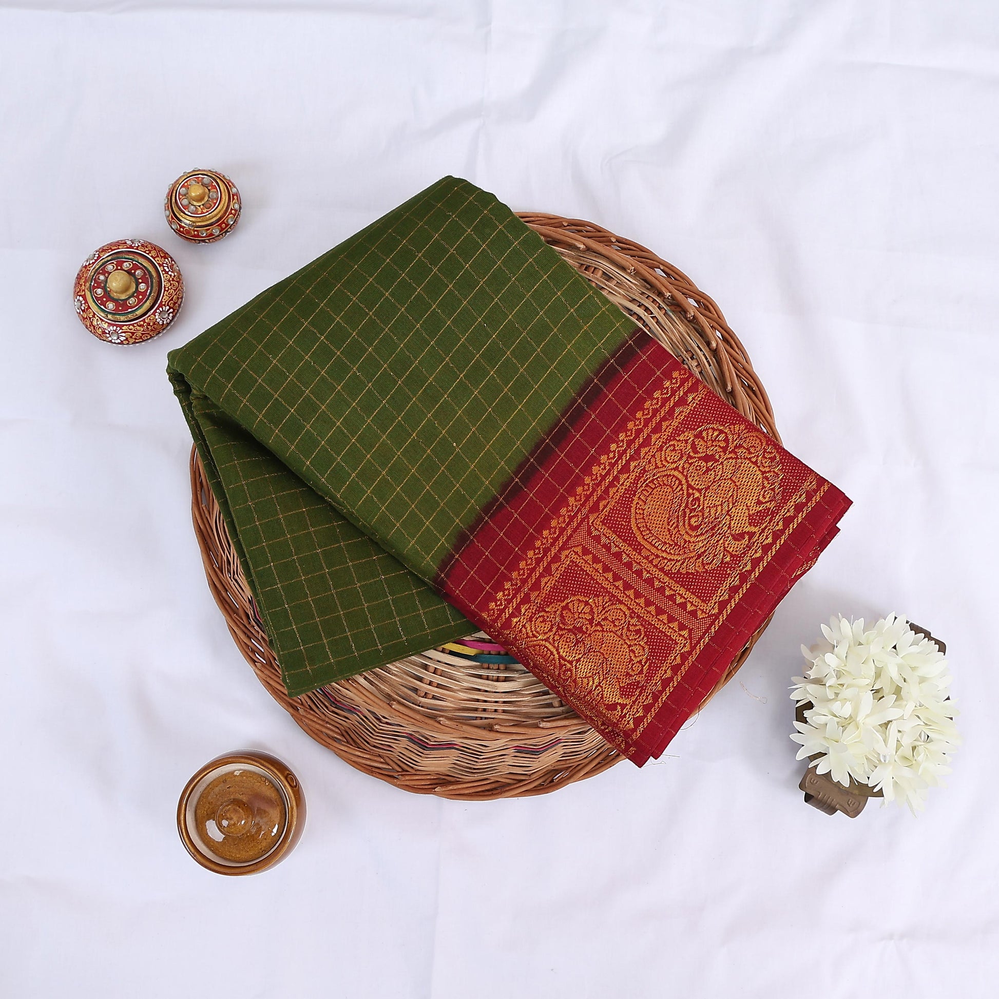 Sungudi cotton saree with gold zari checks body and green peacock motif border folded top view on wicker basket