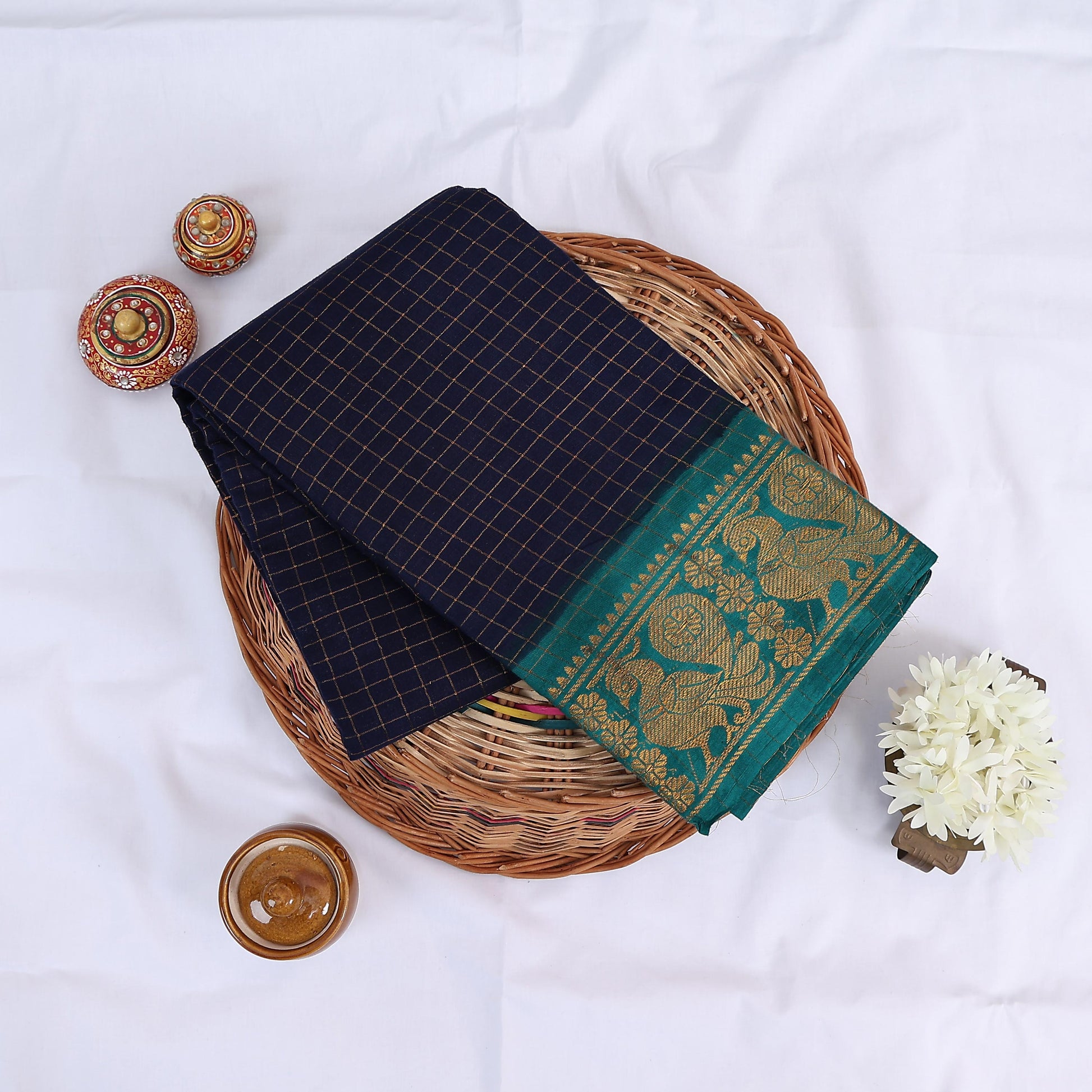 Sungudi cotton saree with gold zari checks body and teal peacock motif border folded top view on wicker basket