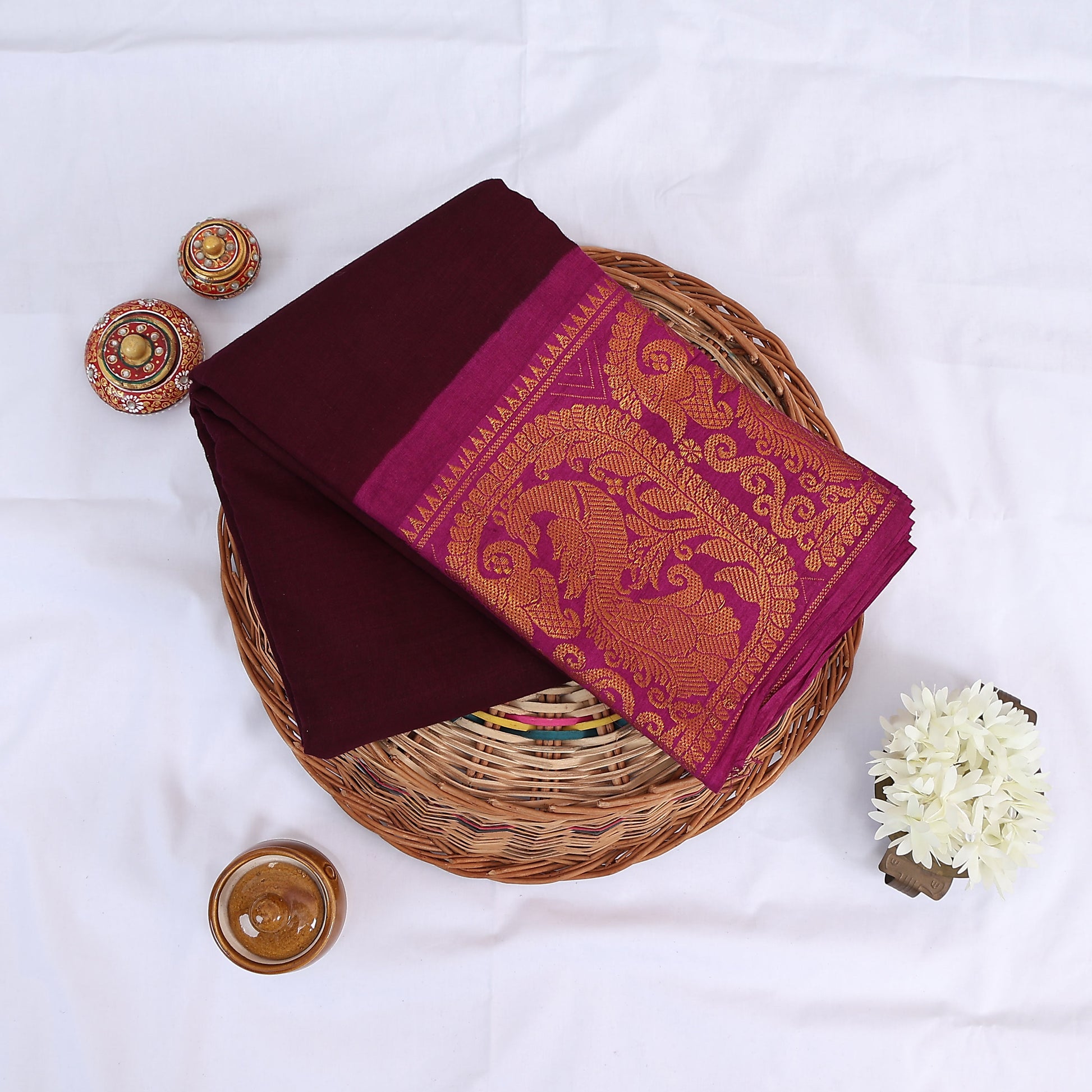 Sungudi cotton saree with gold zari woven border maroon and magenta folded top view on wicker basket