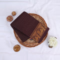 Sungudi cotton saree with gold zari checks body and dark maroon peacock motif border folded top view on wicker basket