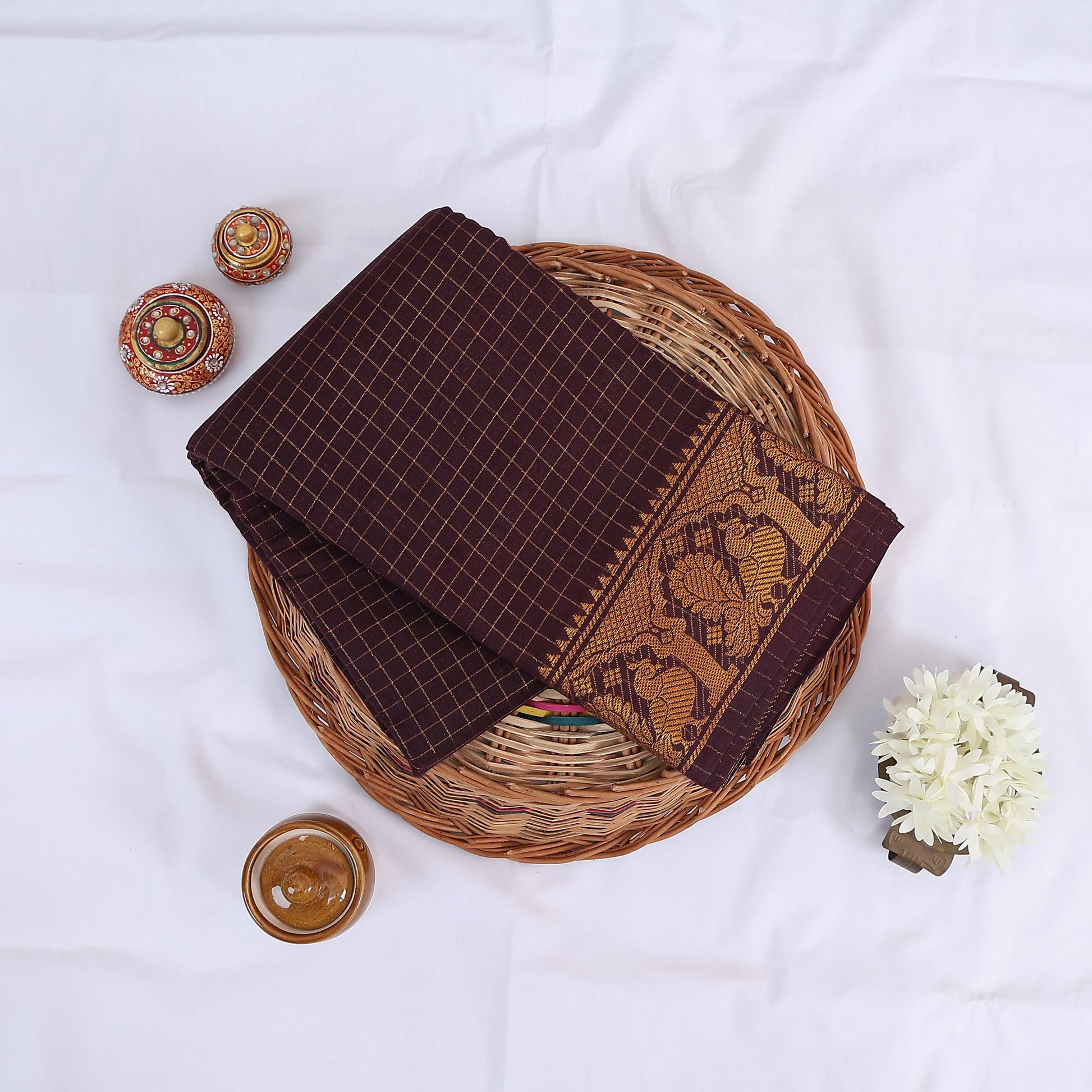 Sungudi cotton saree with gold zari checks body and dark maroon peacock motif border folded top view on wicker basket