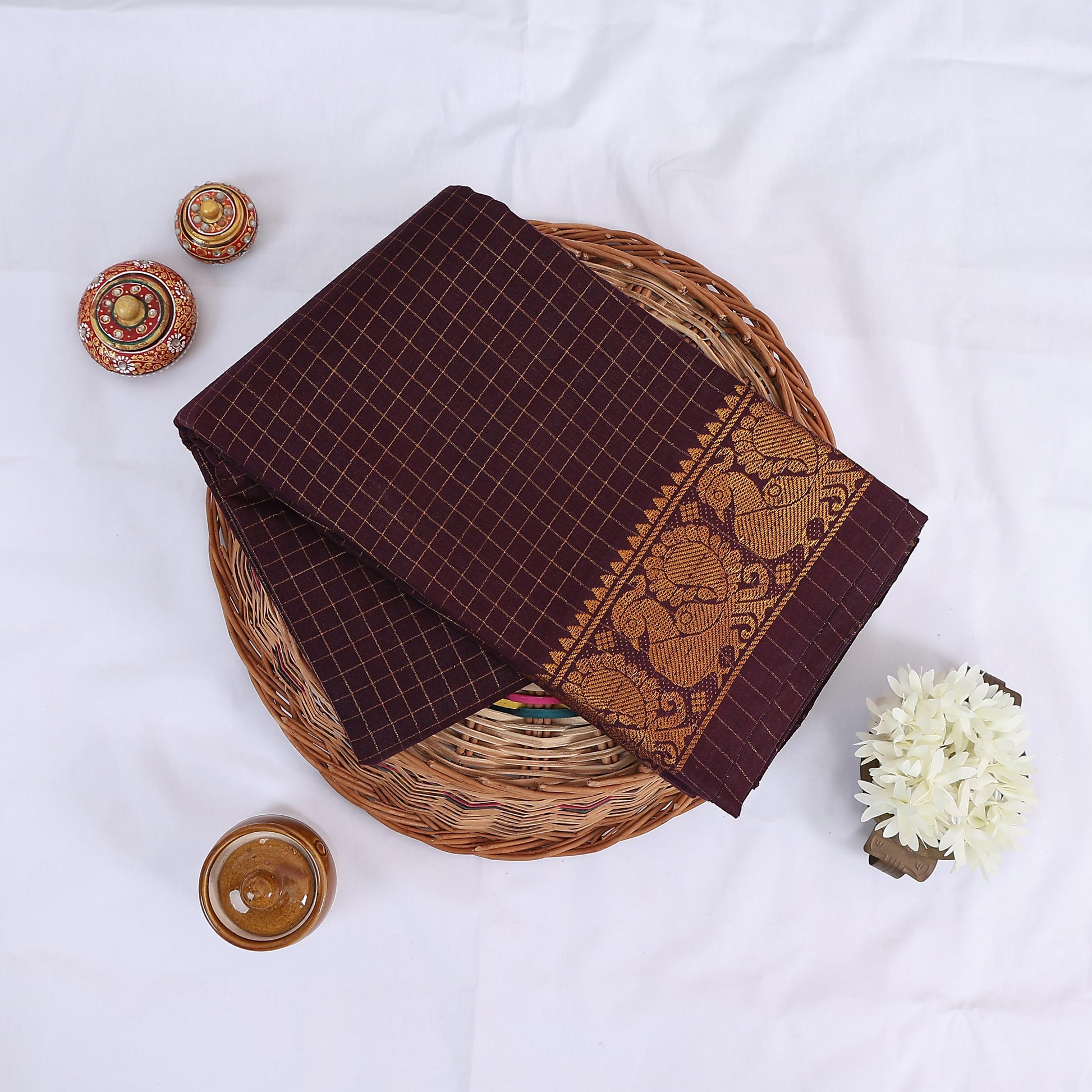 Sungudi cotton saree with gold zari checks body and maroon peacock motif border folded top view on wicker basket