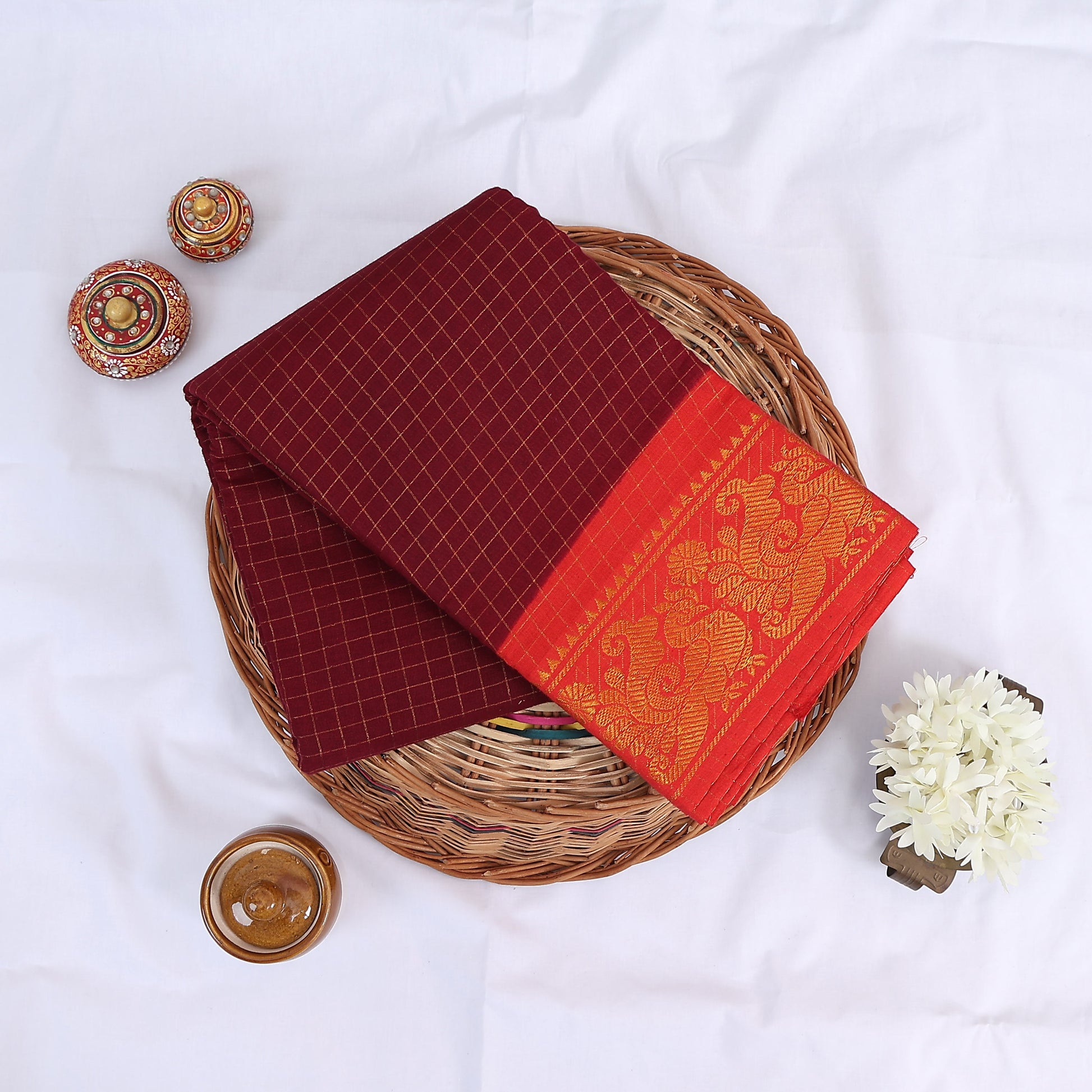 Sungudi cotton saree with gold zari checks body and red peacock motif border folded top view on wicker basket