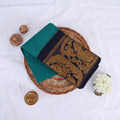Sungudi cotton saree in teal green with navy blue border and gold woven peacock motifs folded flat lay view on wicker basket