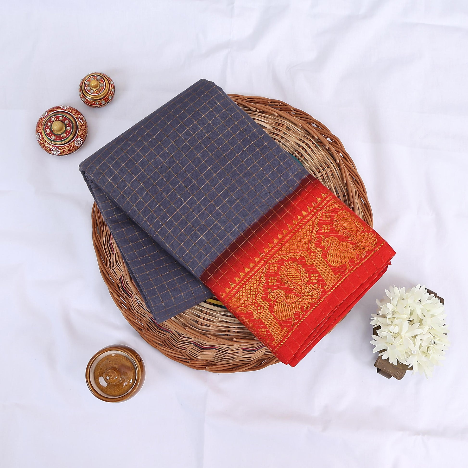 Sungudi cotton saree with gold zari checks body and red peacock motif border folded top view on wicker basket