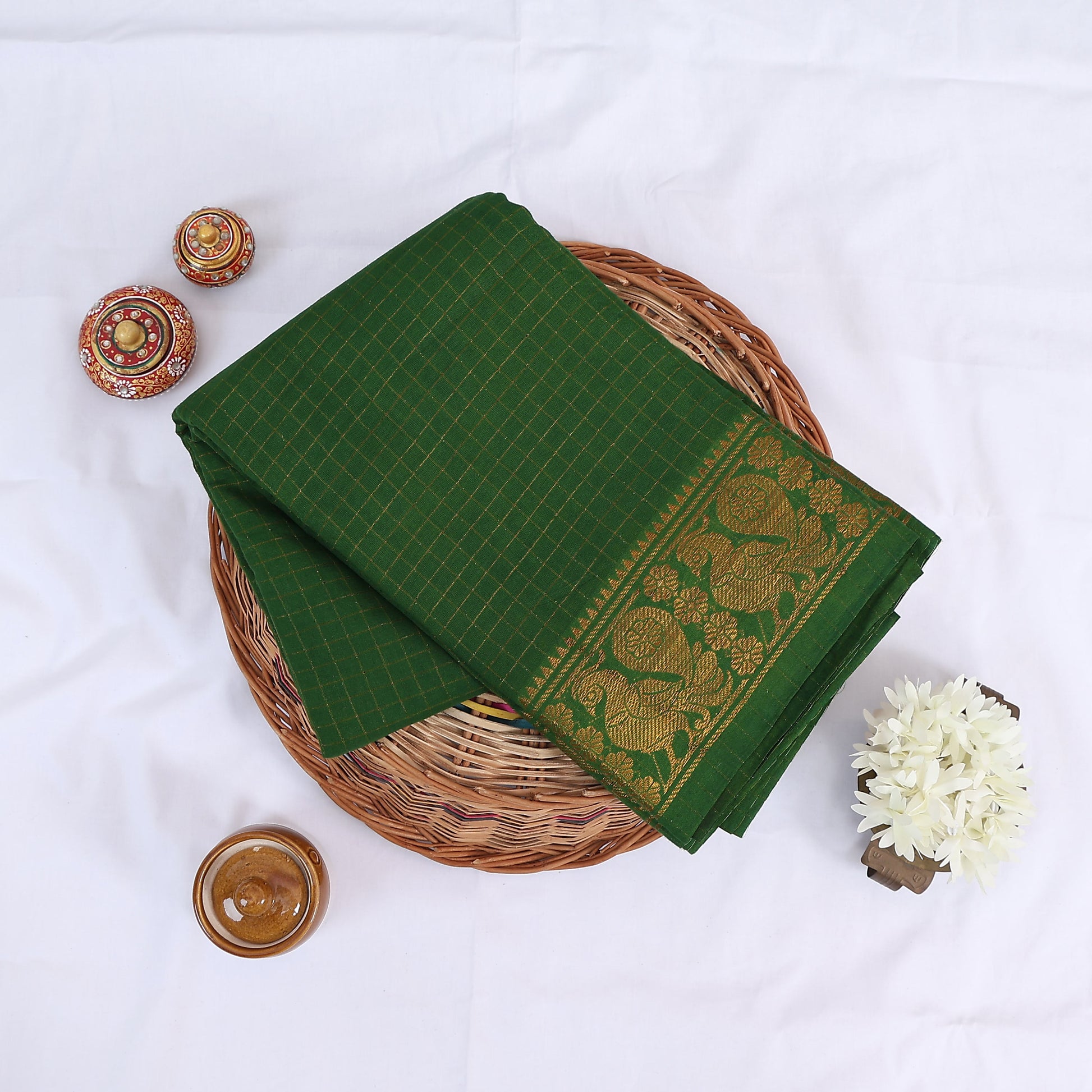 Sungudi cotton saree with gold zari checks body and green peacock motif border folded top view on wicker basket