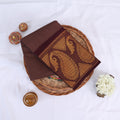 Sungudi cotton saree in brown with maroon border and gold paisley woven design folded flat lay view on wicker basket