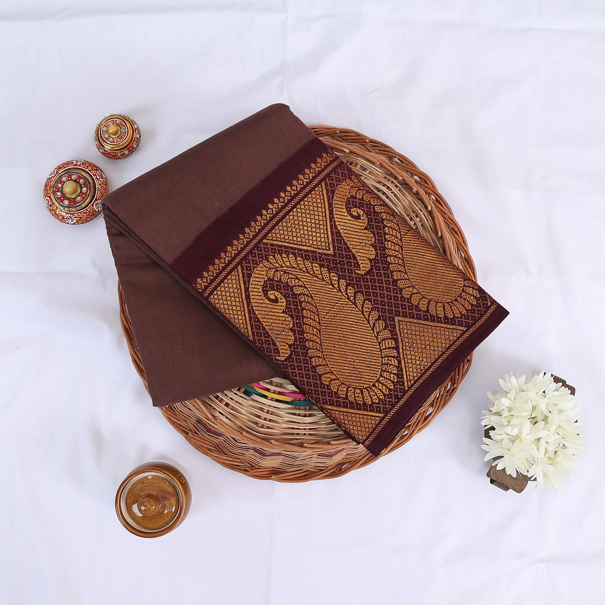 Sungudi cotton saree in brown with maroon border and gold paisley woven design folded flat lay view on wicker basket